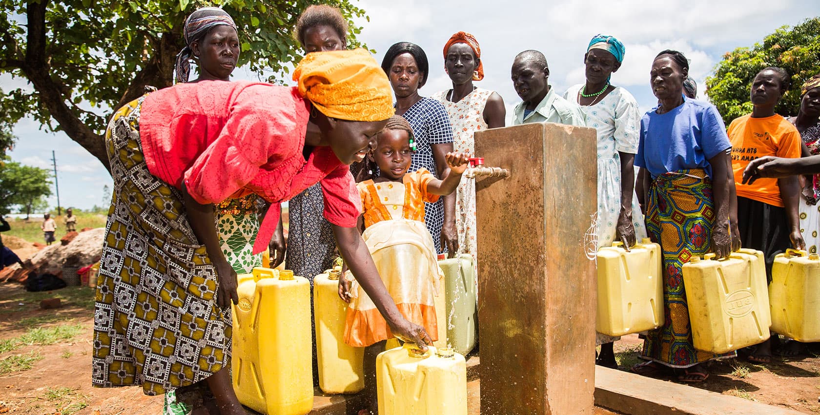 Women and children line up at an outdoor water pump.